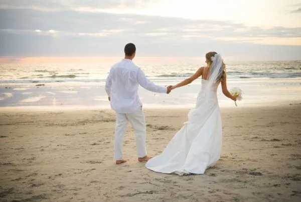 Bride and groom holding hands beside the sea at sunset